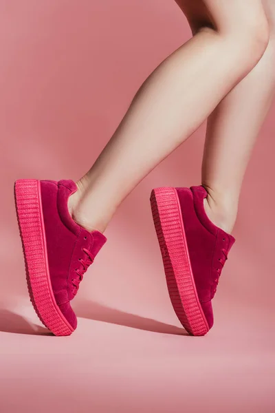 Recortado disparo de chica en zapatillas de deporte con estilo de pie en los dedos del pie sobre fondo rosa - foto de stock