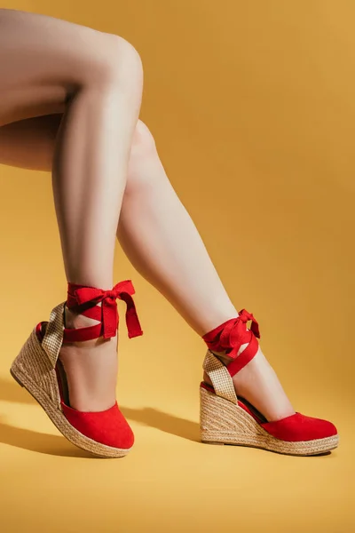 Tiro recortado de piernas de mujer en sandalias de plataforma con estilo sobre fondo amarillo - foto de stock