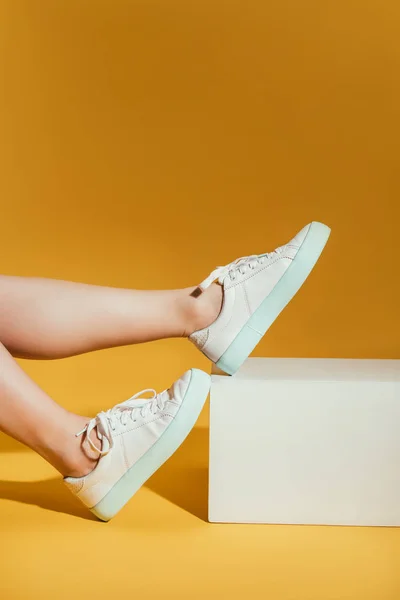 Imagen recortada de pies de mujer en zapatillas de deporte con estilo sobre fondo amarillo - foto de stock