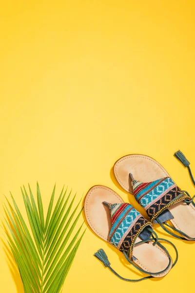 Top view of palm leaf and stylish female sandals on yellow background — Stock Photo