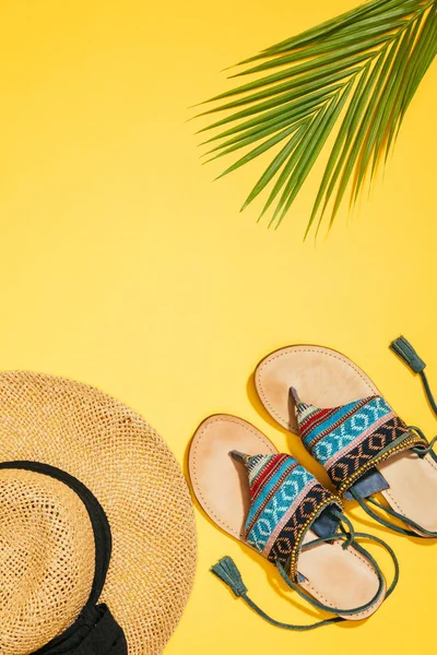 Elevated view of straw hat, palm leaf and stylish female sandals on yellow background — Stock Photo