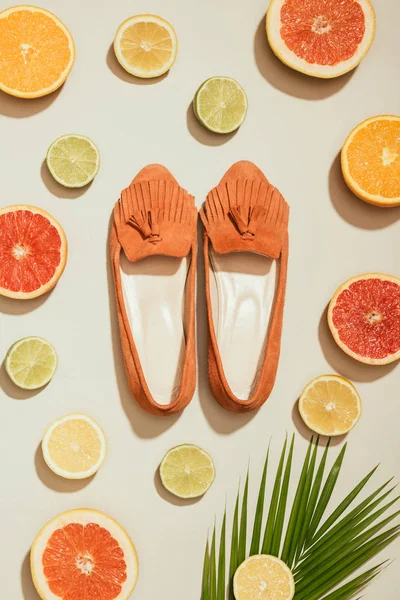 Vista dall'alto di foglia di palma, fette di vari agrumi ed eleganti scarpe da donna pantofola su sfondo bianco — Foto stock