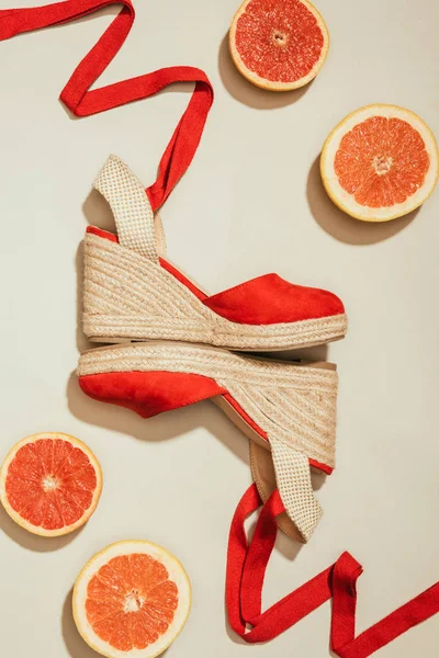 Vue de dessus de sandales plates-formes féminines élégantes entre des tranches de pamplemousse sur fond blanc — Photo de stock