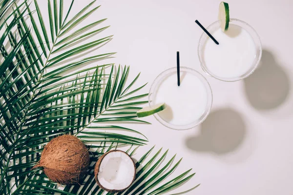 Vista superior de cocos orgânicos, folhas de palma verde e coquetéis de coco em copos com palhas de bebida em branco — Fotografia de Stock