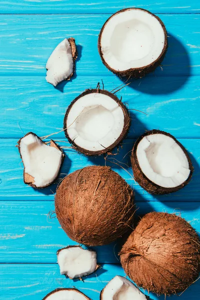 Draufsicht auf ganze Kokosnüsse und -stücke auf blauem Holztisch — Stockfoto