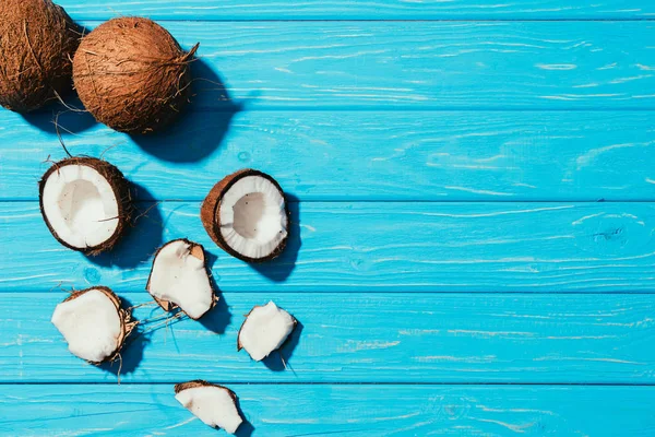 Top view of whole coconuts and pieces on turquoise wooden surface — Stock Photo