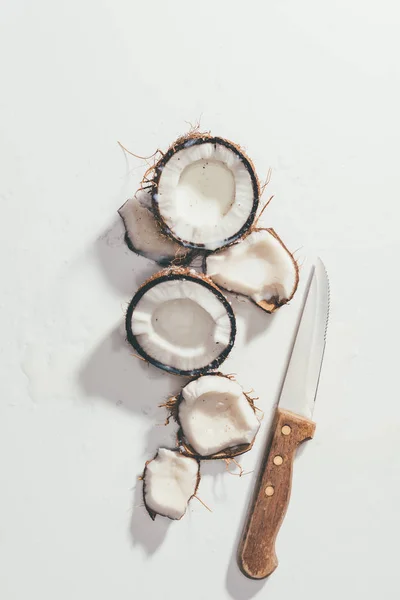 Draufsicht auf natürliche gesunde Kokosnussstücke und Messer auf Weiß — Stockfoto