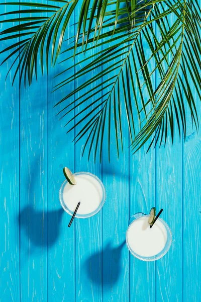 Vista superior de cocteles de coco en vasos y hojas de palma verde sobre mesa de madera turquesa - foto de stock