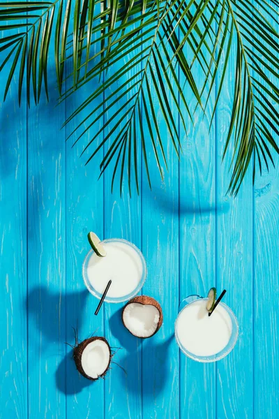 Vue de dessus des cocktails de noix de coco dans des verres et noix de coco craquelée sur le dessus de table bleu — Photo de stock