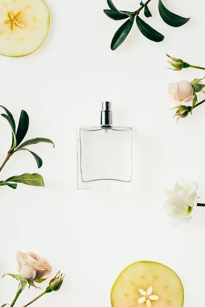 Vue du dessus du flacon de parfum en verre entouré de fleurs et de tranches de pomme isolées sur blanc — Photo de stock