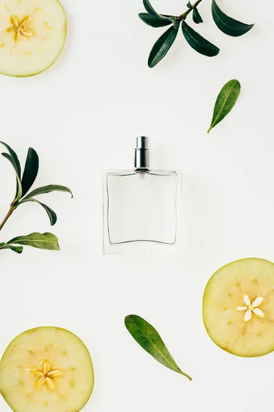 Vista superior de frasco de vidrio de perfume rodeado de ramas verdes y rodajas de manzana aisladas en blanco — Stock Photo