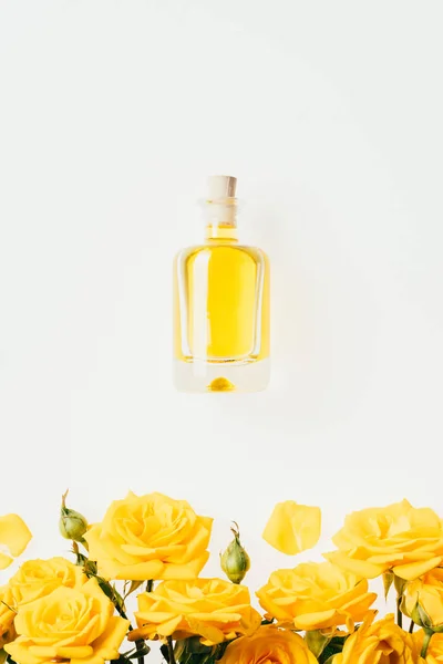 Draufsicht auf eine Flasche Parfüm und gelbe Rosen auf weißem Grund — Stockfoto