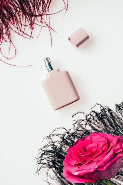 Vista superior de la botella de perfume con pluma y rosa sobre blanco - foto de stock