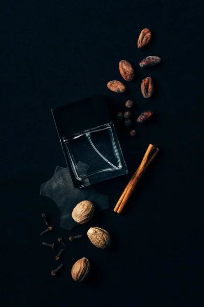 Vue du dessus du flacon en verre de parfum entouré d'épices aromatiques sur noir — Photo de stock