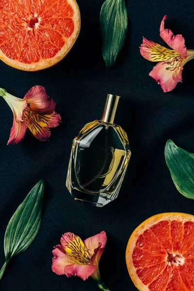 Top view of bottle of perfume surrounded with alstroemeria flowers and grapefruit slices on black — Stock Photo