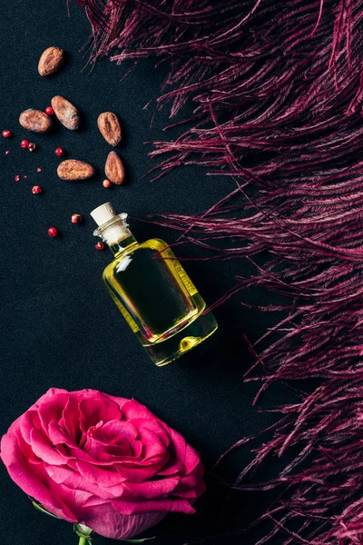 Vue du dessus du flacon de parfum avec plume rouge et bouton de rose sur noir — Photo de stock