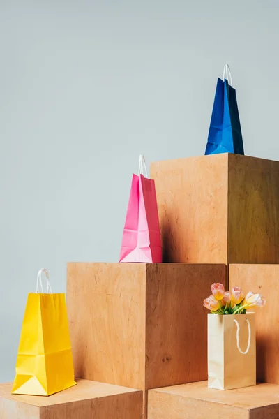 Bolsas de compras de colores y tulipanes en soportes de madera aislados en blanco, concepto de venta de verano - foto de stock