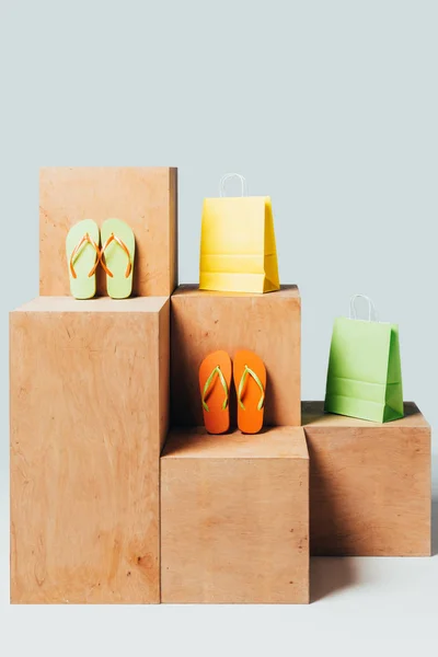 Цветные бумажные пакеты и шлепанцы на деревянных стендах, концепция летней продажи — стоковое фото