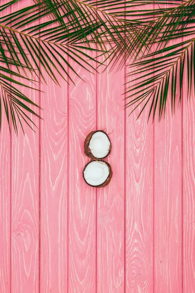 Вид сверху наполовину кокосовых и пальмовых листьев на розовую деревянную поверхность — стоковое фото
