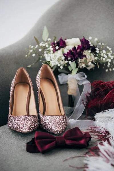 Vue rapprochée des chaussures de mariée, noeud papillon marié, bouquet de mariage et plumes pour mariage rustique sur fauteuil — Photo de stock