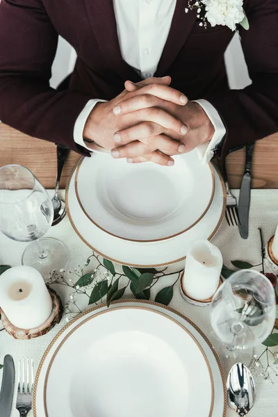 Tiro recortado del novio en traje sentado en la mesa servida, concepto rústico de la boda - foto de stock