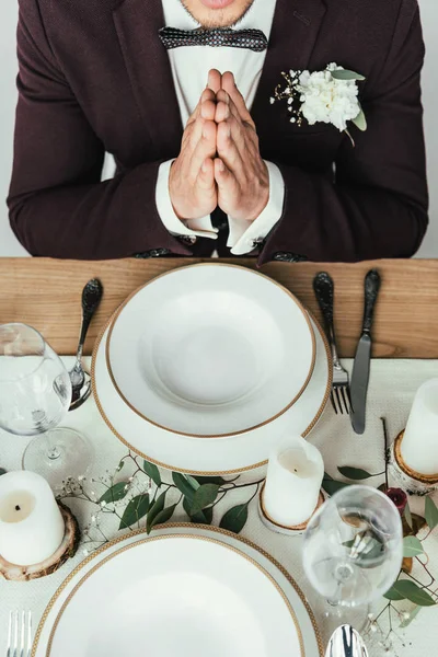 Cropped shot of groom in suit praying while sitting at served table, rustic wedding concept — Stock Photo