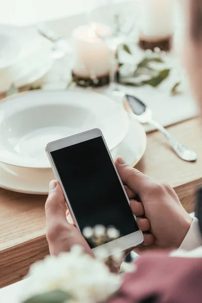 Ritagliato colpo di sposo utilizzando smartphone al tavolo rustico servito — Foto stock