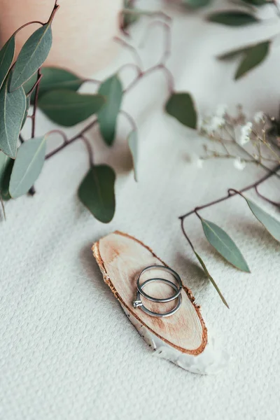 Vista de cerca de los anillos de boda en tablero decorativo de madera y eucalipto en la mesa - foto de stock