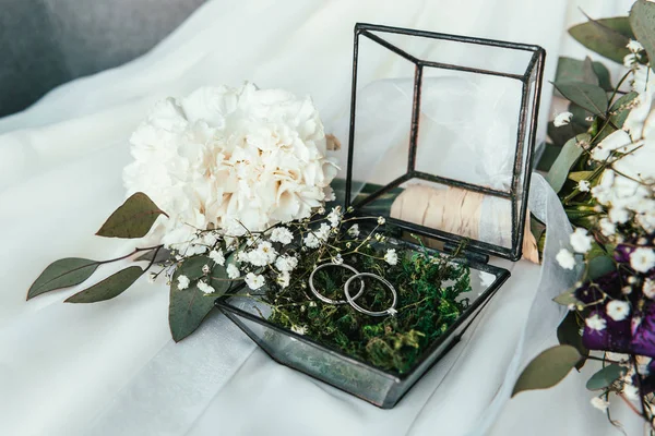 Close up view of white flowers, wedding rings in rustic box with plants inside — Stock Photo