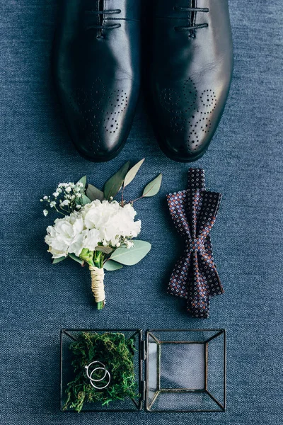 Flache Lage mit Anordnung der Bräutigamsschuhe, Fliege, Corsage und Trauringe für rustikale Hochzeit auf blauem Hintergrund — Stockfoto