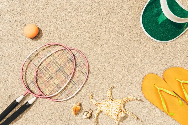 Vista superior do equipamento de badminton, boné e chinelos na areia — Fotografia de Stock