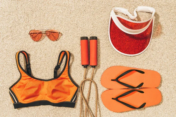 Vista superior de la cuerda de salto arreglada, ropa deportiva, gafas de sol, gorra y chanclas en la arena - foto de stock