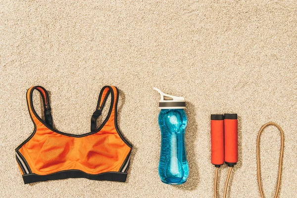 Top view of arranged sportswear, skipping rope and water bottle on sand — Stock Photo
