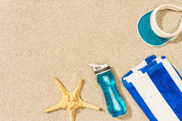 Flat lay com estrela do mar, garrafa de água, toalha e tampa dispostas na areia — Fotografia de Stock