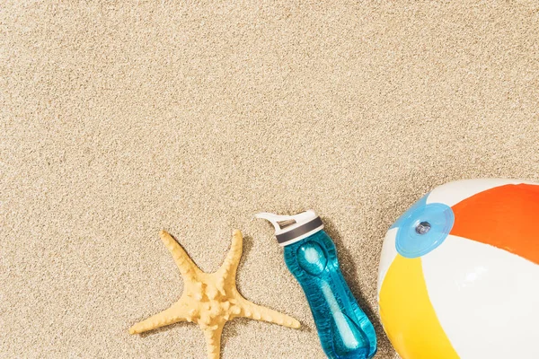 Flat lay with arranged water bottle, sea star and beach ball on sand — Stock Photo