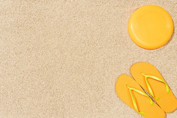 Vista superior de chanclas amarillas y frisbee sobre arena - foto de stock