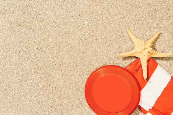 Top view of sea star, red frisbee and towel on sand — Stock Photo