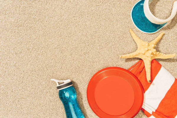 Flat lay with water bottle, towel, cap, frisbee and sea star on sand — Stock Photo