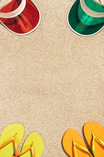 Top view of arranged colorful caps and flip flops on sand — Stock Photo
