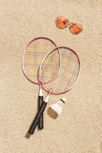Top view of arranged badminton equipment and sunglasses on sand — Stock Photo