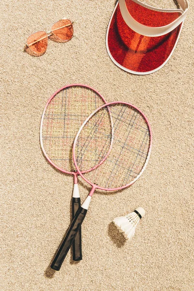 Top view of badminton equipment, sunglasses and cap on sand — Stock Photo