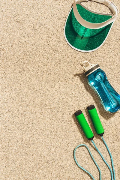 Top view of arranged cap, water bottle and jump rope on sand — Stock Photo