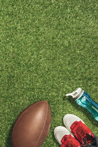 Acostado plano con zapatillas de deporte, pelota de rugby y botella de agua en el césped verde - foto de stock