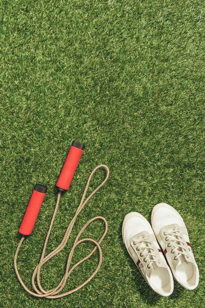 Top view of arranged sneakers and skipping rope on green grass — Stock Photo