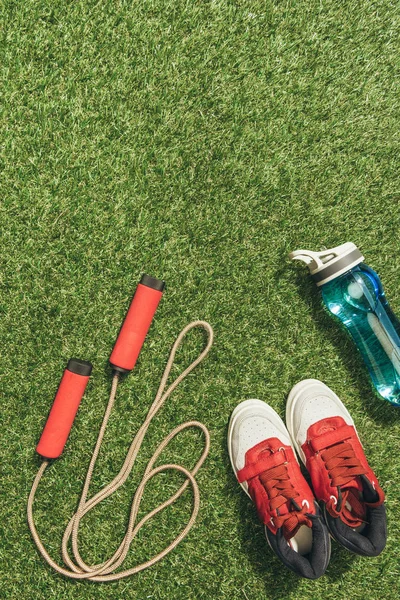 Top view of arranged water bottle, skipping rope and sneakers on green grass — Stock Photo