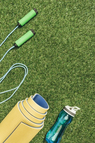 Vista superior do tapete amarelo arranjado, pulando corda e garrafa de água na grama verde — Fotografia de Stock