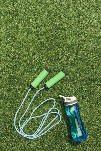 Vue de dessus de la bouteille d'eau arrangée et corde à sauter sur l'herbe verte — Photo de stock