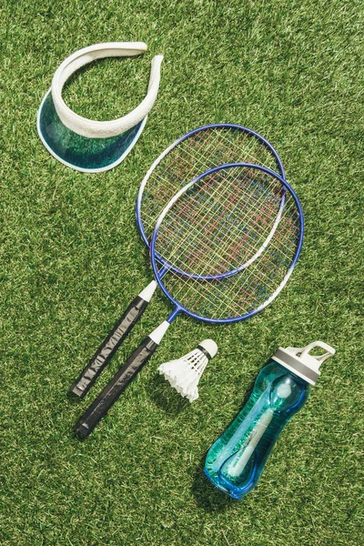 Top view of badminton equipment, water bottle and cap on green grass — Stock Photo