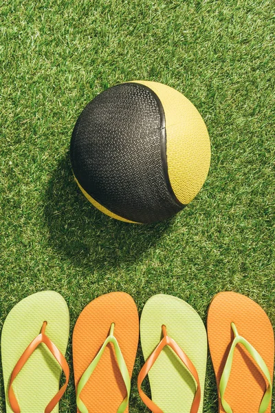 Top view of medicine ball and colorful flip flops on green grass — Stock Photo