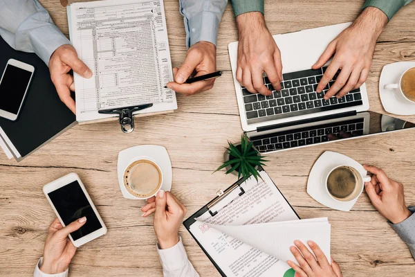 Vue d'ensemble des partenaires commerciaux travaillant avec des documents, un ordinateur portable et un smartphone à table, vue recadrée — Photo de stock